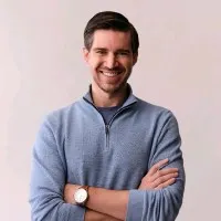 Charley Moore SVP Finances & Operations, Mack Weldon, smiling with dark hair wearing a gray quarter-zip sweater and watch with arms crossed.
